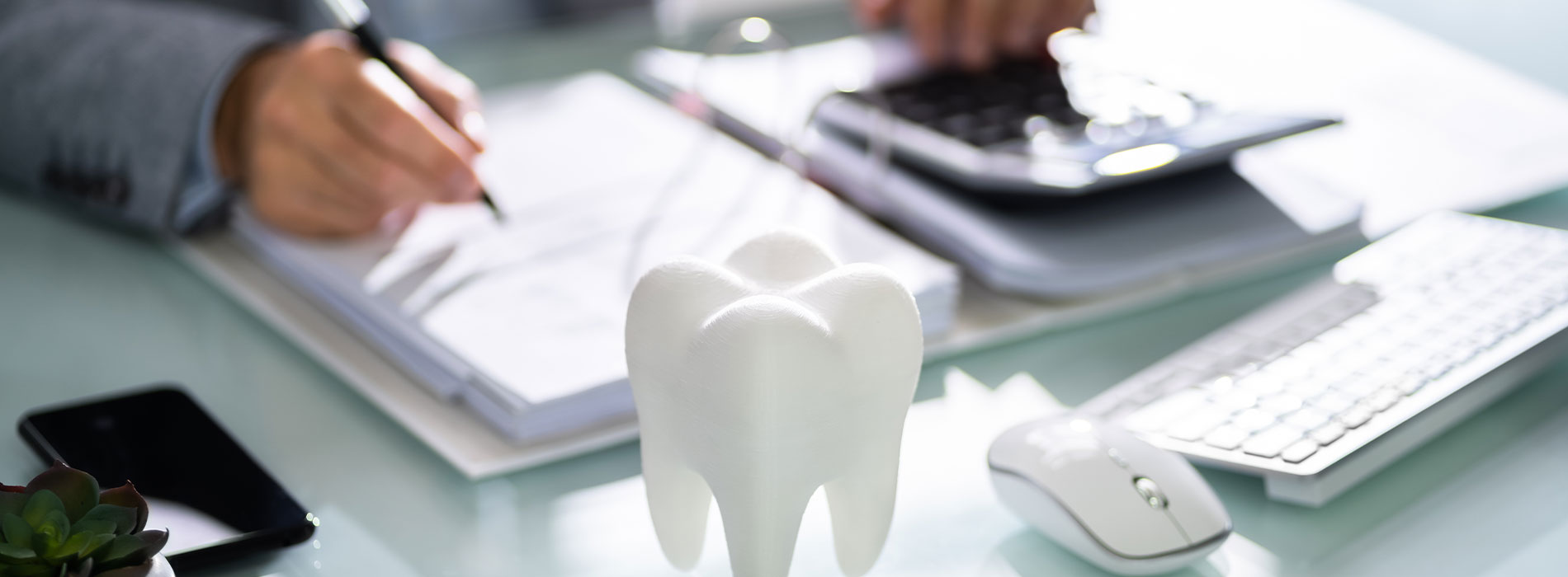 The image shows a person sitting at a desk with their hands on a keyboard, surrounded by various office items such as a phone, notebooks, and a mouse.
