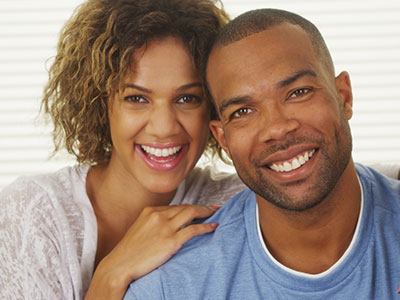 A man and woman are smiling at the camera, posing for a portrait with a warm and happy expression.