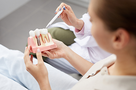 A person holding a model set of teeth while seated in a dental office chair.